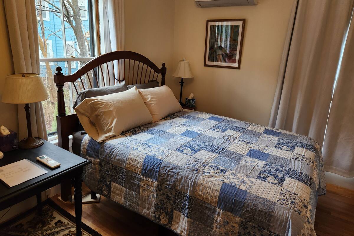 Une chambre à coucher avec un lit en bois, une table de chevet, une lampe, un tableau encadré au mur et un appareil de climatisation.