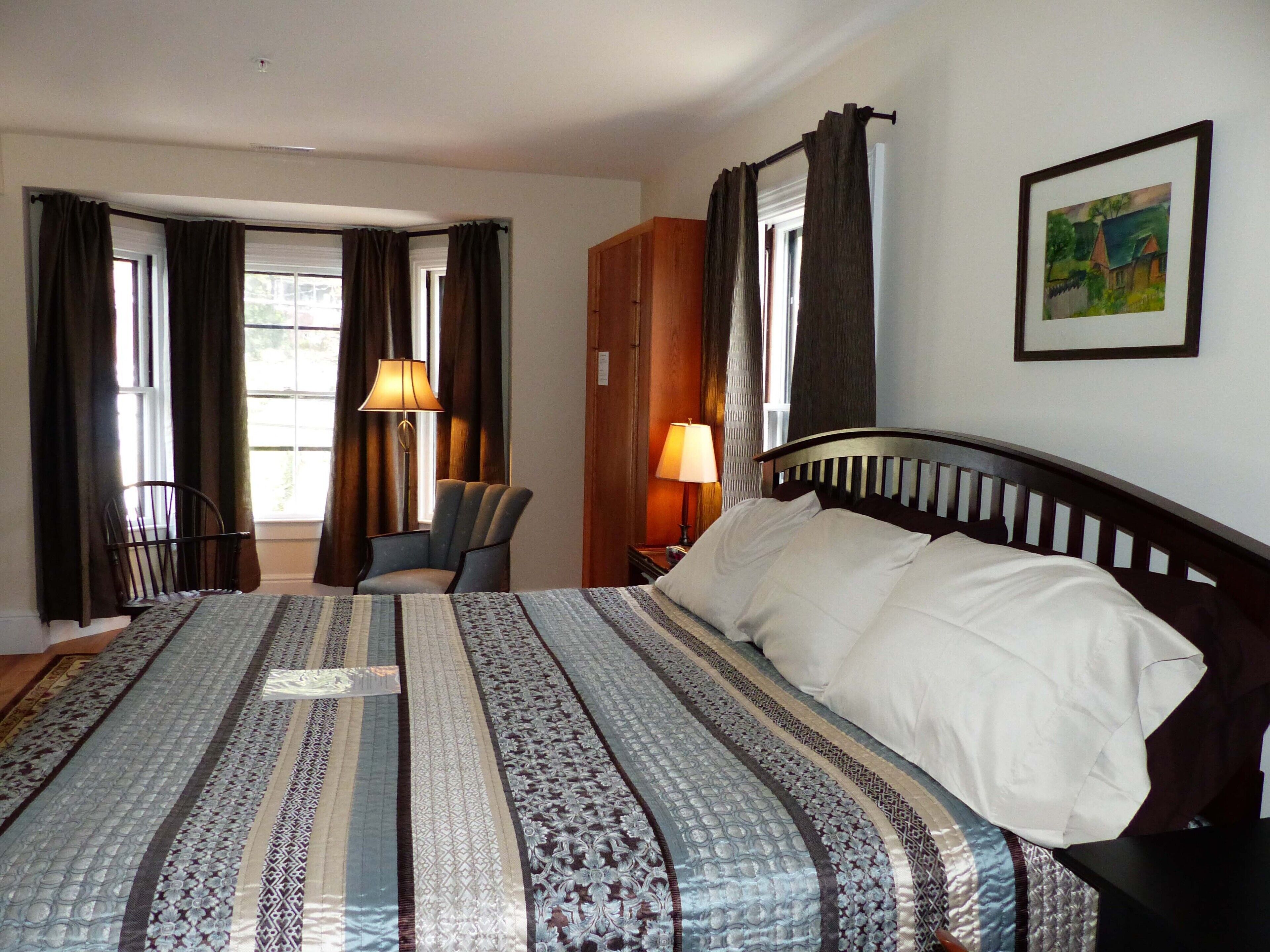 A hotel room with a large bed, a chair, a desk, and a painting on the wall.
