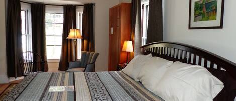 A hotel room with a large bed, a chair, a desk, and a painting on the wall.