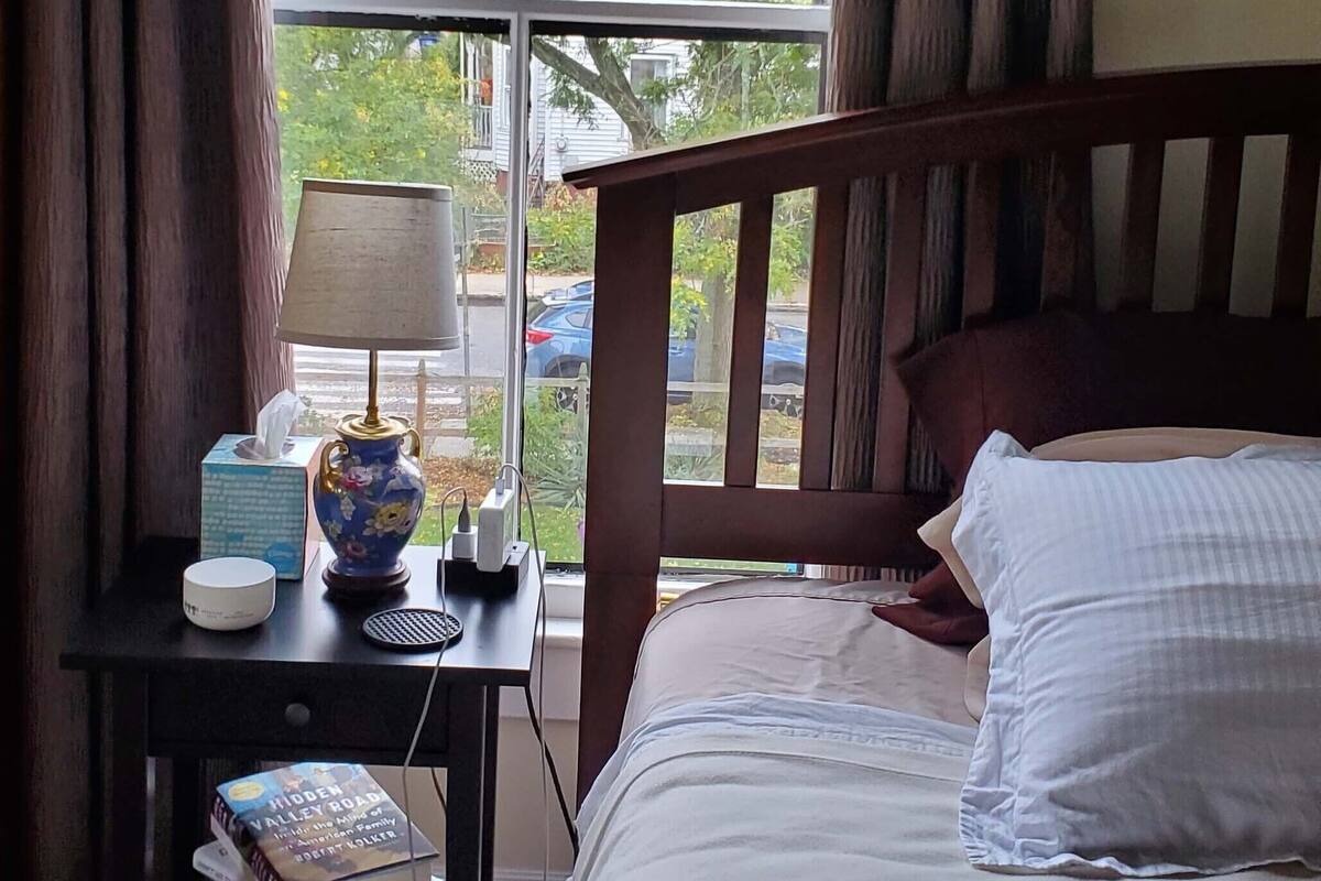 Une chambre à coucher avec une tête de lit en bois, une table de chevet avec une lampe, un vase et des livres.