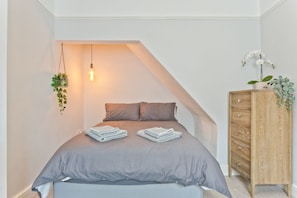 Een slaapkamer met een bed, een hangplant, een houten dressoir en een lamp.