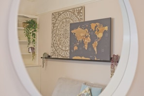Een kamer met een wereldkaart en een decoratief paneel aan de muur, een plank met planten en een bank met kussens.
