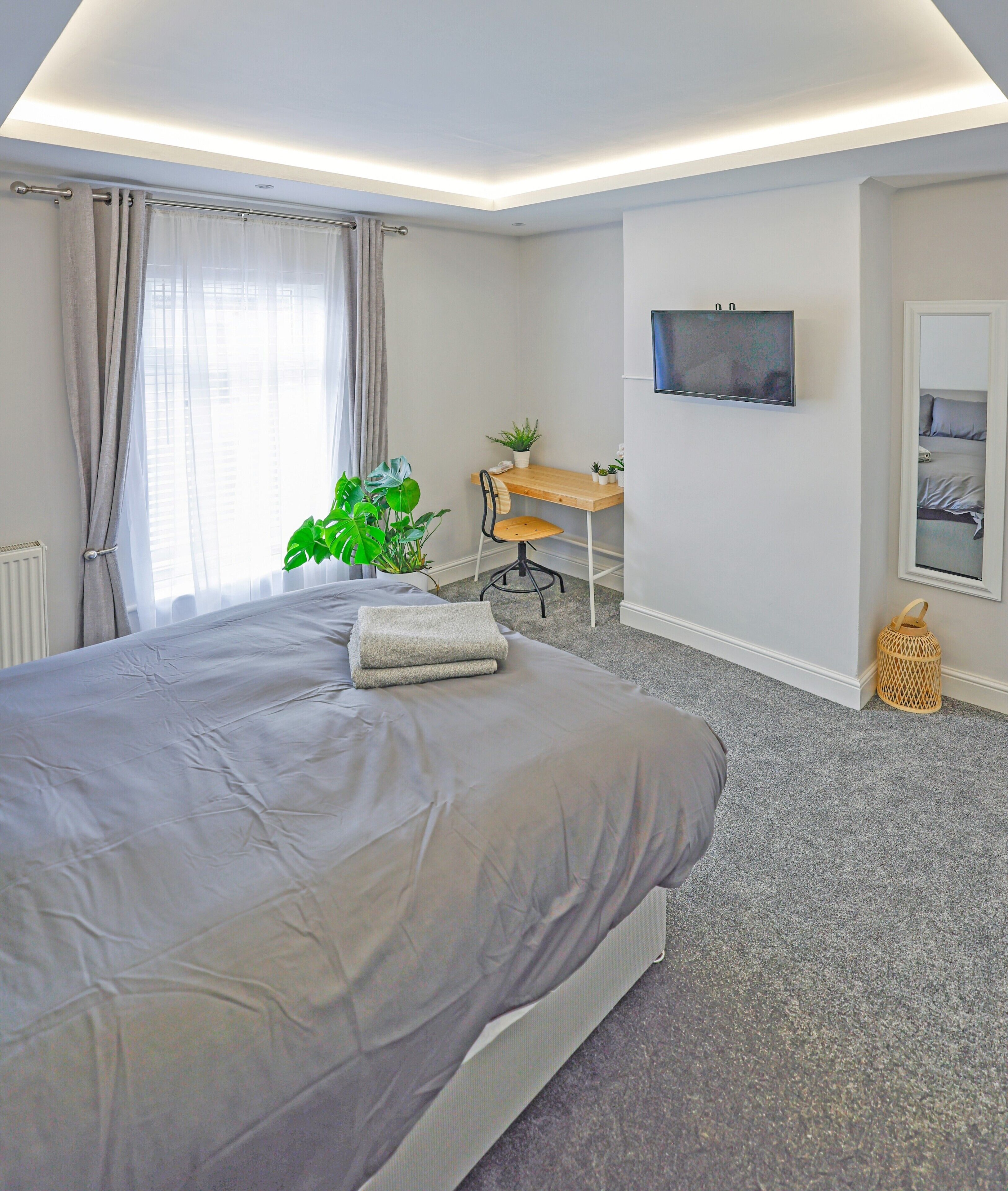 A bedroom with a large bed, a desk, a chair, a television, and a plant.