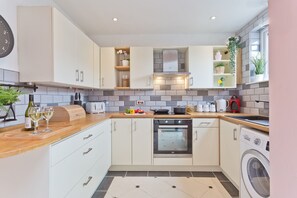 A modern kitchen with white cabinets, a built-in oven, a washing machine, and a variety of appliances and utensils on the countertops.