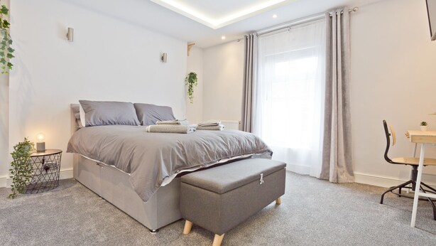 A modern bedroom with a bed, bedside table, bench, and a small desk with a chair. - Malleus House (Barrow-in-Furness)