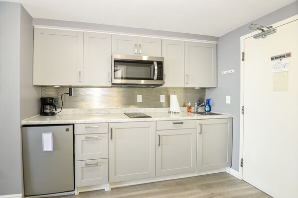 A compact kitchen with a built-in microwave, a coffee maker, and a dishwasher. - Ocean Views clean room with small balcony no amenities until end of Nov (Daytona Beach)
