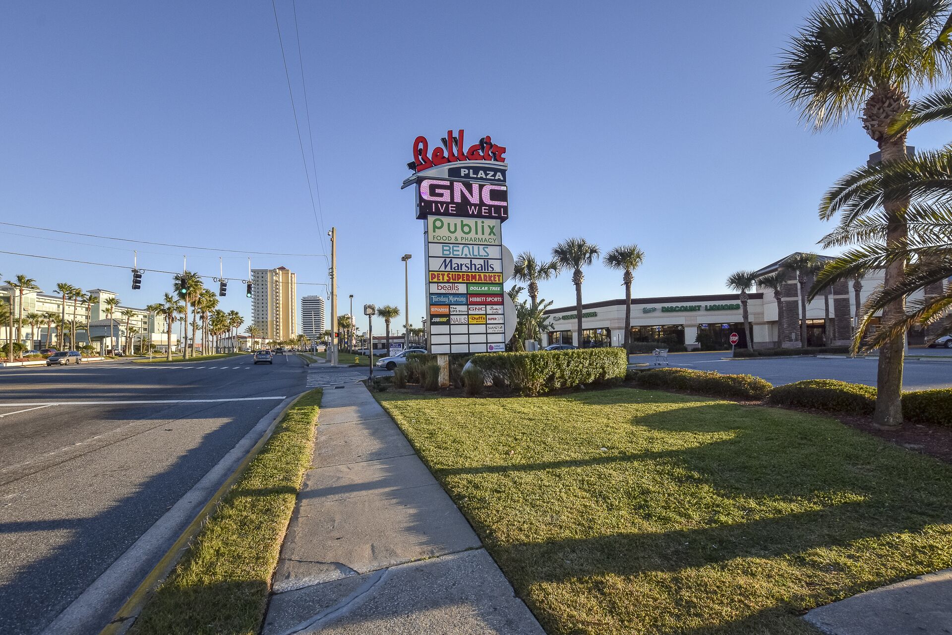 A street view with a large sign for Bellair Plaza, GNC, Publix, and other businesses.