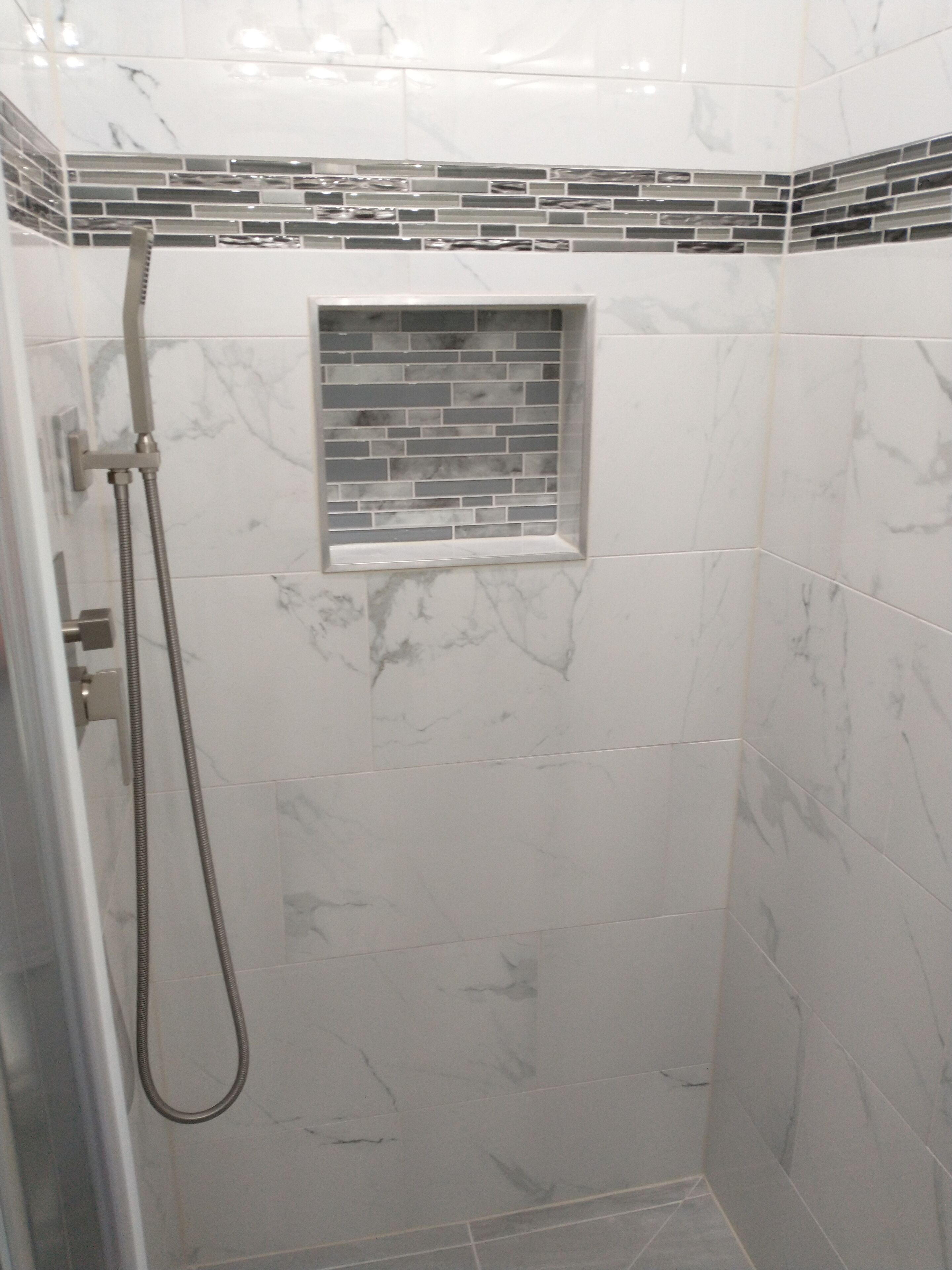 A shower with a handheld showerhead, a small window with a mosaic tile design, and a tiled wall with a marble pattern.