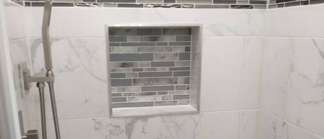 A shower with a handheld showerhead, a small window with a mosaic tile design, and a tiled wall with a marble pattern.