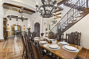 A dining area with a long wooden table set for a meal, a staircase with ornate railings, and a chandelier. - The Spanish Castle | West facing pool, SPA and views of Jack Nicklaus Golf Course (Kissimmee)