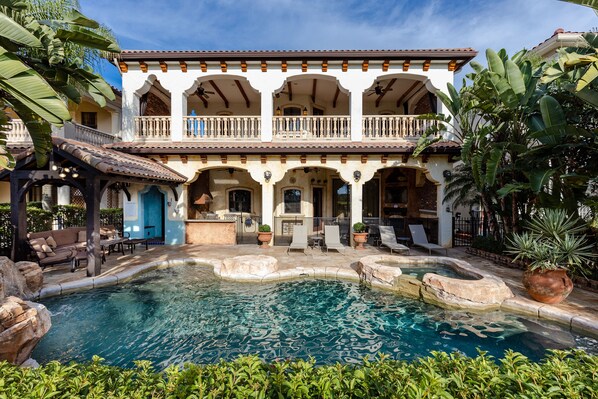 A two-story building with a swimming pool, outdoor seating, and tropical plants. - The Spanish Castle | West facing pool, SPA and views of Jack Nicklaus Golf Course (Kissimmee)