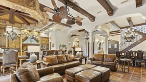 A spacious living area with leather sofas, a dining table, and a staircase. - The Spanish Castle | West facing pool, SPA and views of Jack Nicklaus Golf Course (Kissimmee)