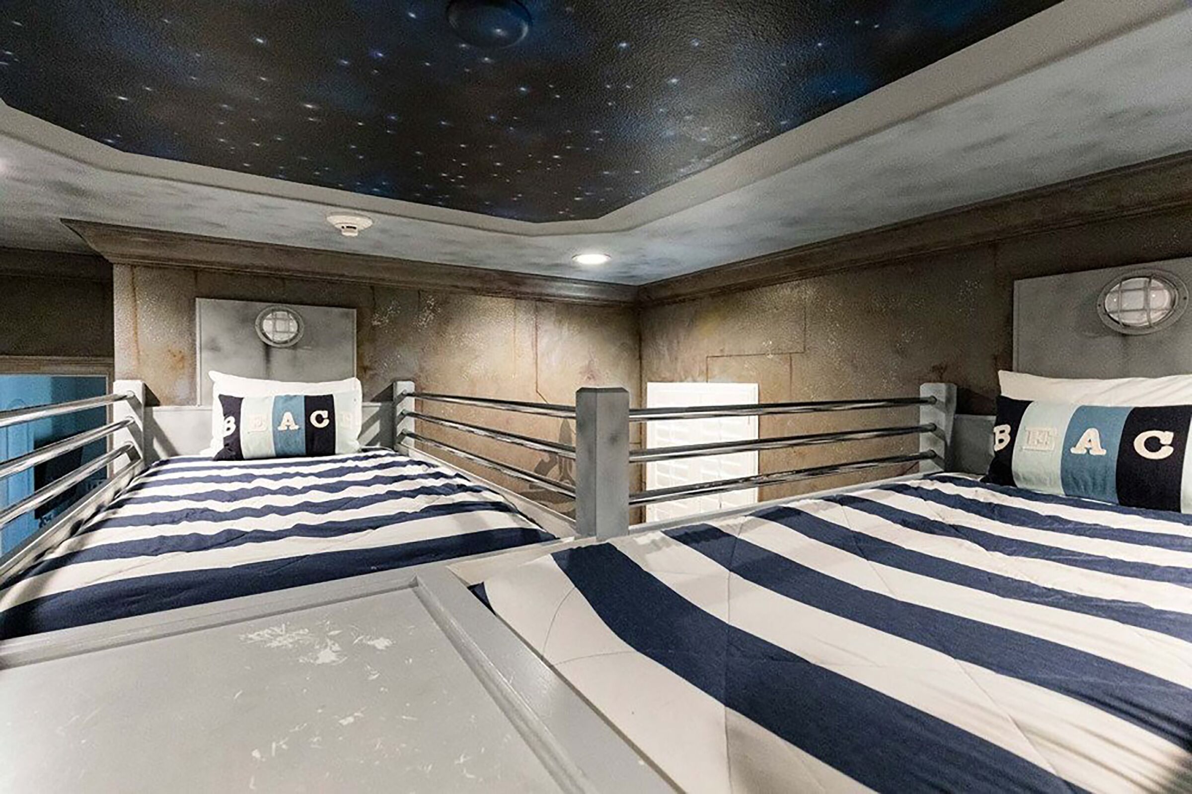A room with bunk beds, a starry ceiling, and a window with a view of the sky.