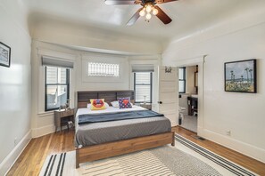 A bedroom with a wooden bed, a ceiling fan, and a view of the bathroom.