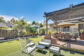 A backyard patio area with outdoor furniture, a pergola, and a variety of potted plants.