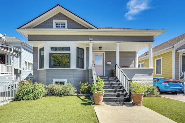 A two-story residential house with a front porch, a staircase leading to the entrance, and a small garden area with potted plants.