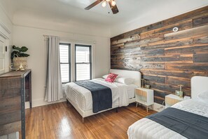 A bedroom with a wooden wall, a bed with white bedding, a bedside table with a lamp, and a window with curtains.