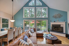 Relax in a spacious living room with a high ceiling, large windows, and a cozy seating area featuring a sofa, chairs, and a fireplace.