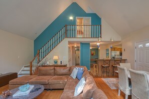 Relax in this spacious living area with a high ceiling, featuring a comfortable sofa, dining table, and kitchen area.