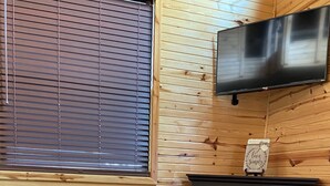 Een gezellige kamer met een houten wand, een open haard, een televisie erboven en een tafel met een decoratieve schaal en boeken.