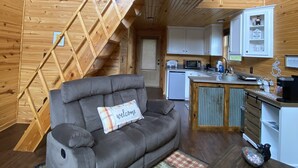 Een blokhut met een slaaploft, een bank met een 'welkom'-kussen, een keuken en een houten trap.