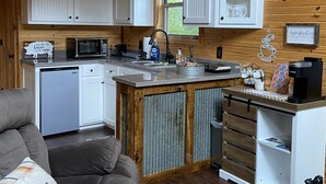 Een compacte keuken met witte kastjes, een magnetron, een spoelbak en een koffiezetapparaat.
