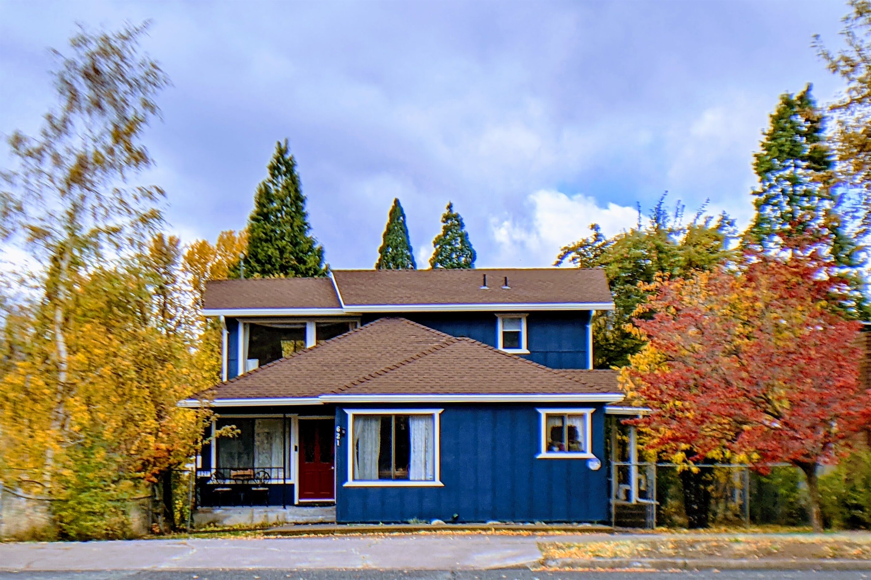 A two-story house with a red door and white trim, surrounded by trees with autumn foliage.