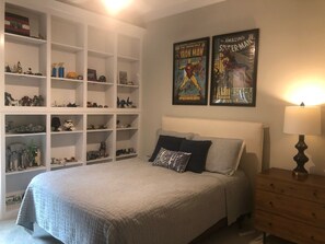 A bedroom with a bed, a dresser, and a shelving unit filled with collectibles.