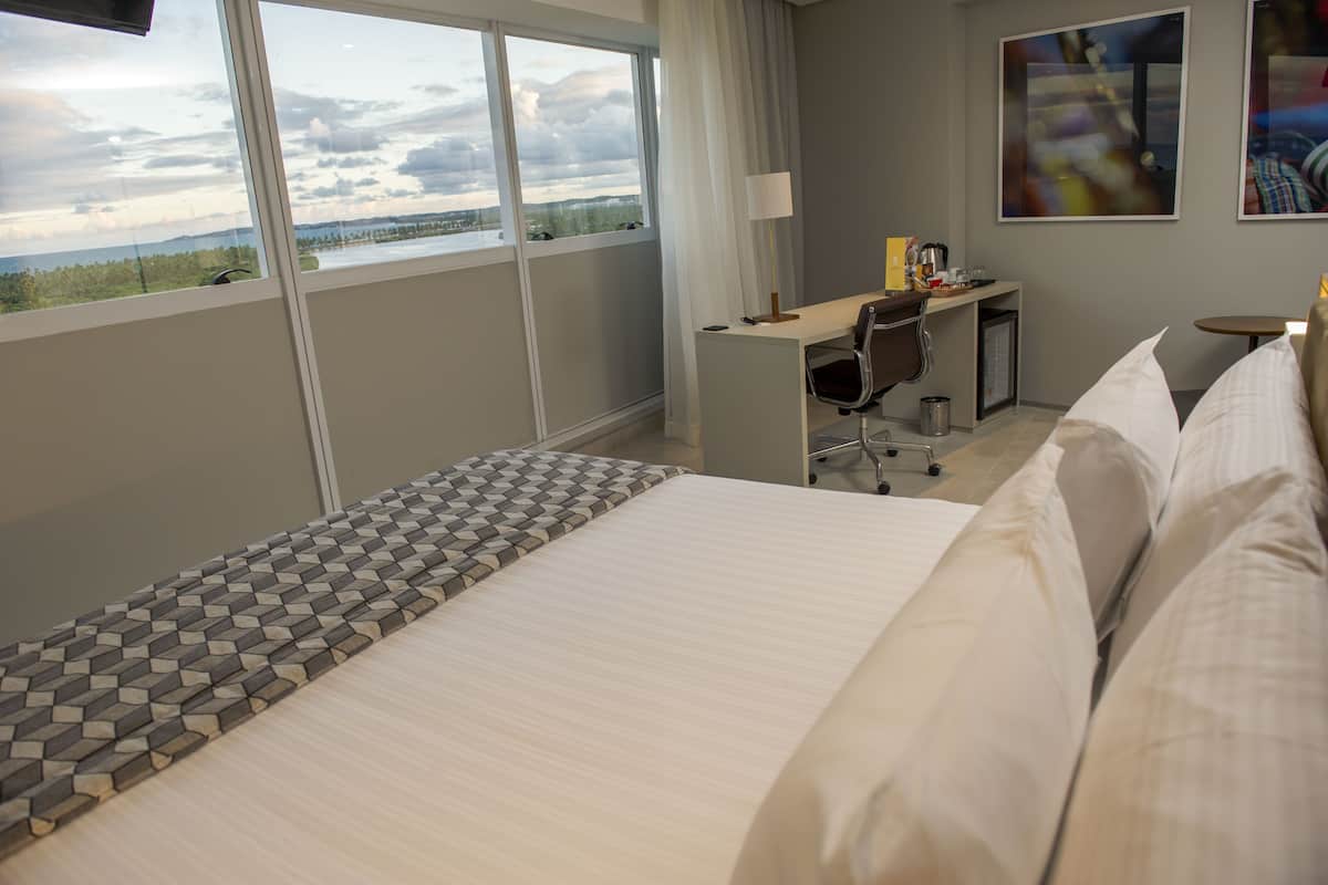 A hotel room with a large bed, a desk, and a view of the outdoors.