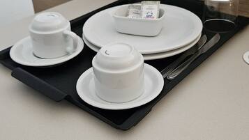 Una bandeja negra con tres tazas y platillos blancos, un cuenco pequeño y un vaso.