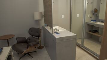 Habitación de hotel moderna con escritorio, silla y zona de ducha con paredes de vidrio.