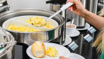 Disposição de buffet com ovos mexidos sendo servidos de uma panela de metal grande.