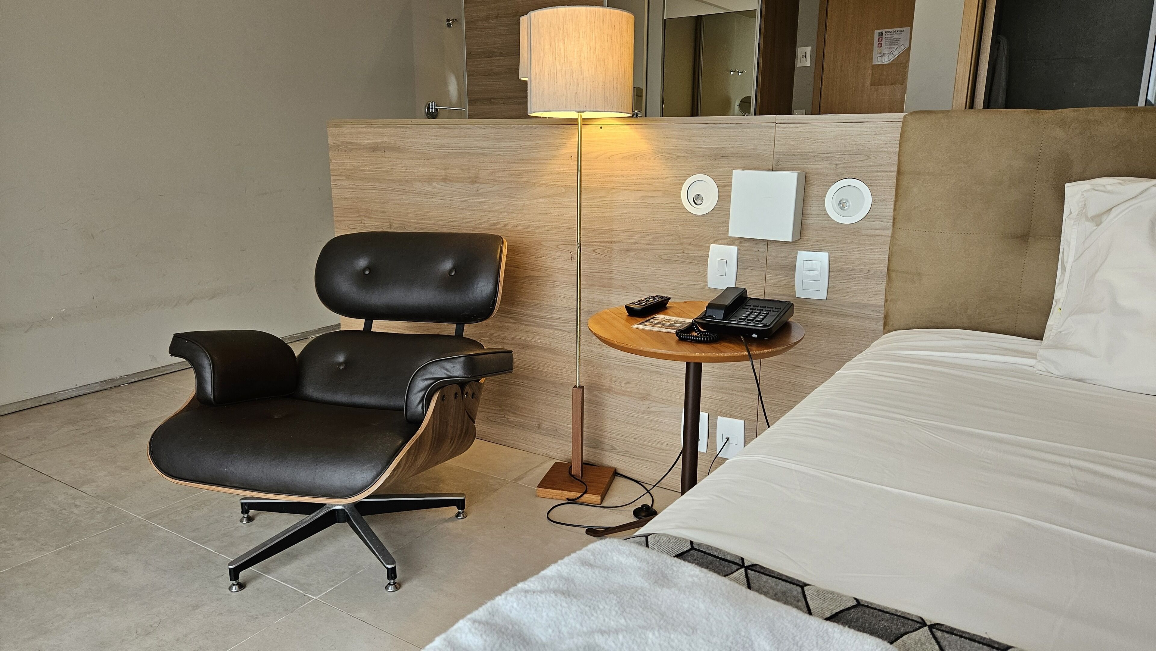 A hotel room with a bed, a desk, a chair, a lamp, and a phone.