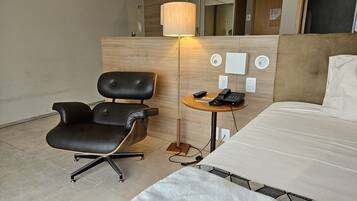 A hotel room with a bed, a desk, a chair, a lamp, and a phone.