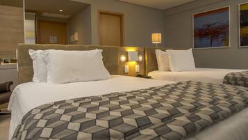 A hotel room with two beds, a large mirror, a bedside table with a lamp, and a painting on the wall.