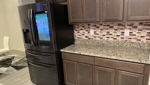 A kitchen with a stainless steel refrigerator, granite countertop, and dark wooden cabinets.
