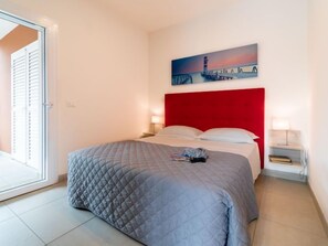 Quarto de hotel com uma cama, cabeceira vermelha, pintura de uma ponte e mesa de cabeceira com abajur.