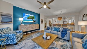 Un salon moderne avec un mur d’accent bleu, un ventilateur de plafond et une vue sur la cuisine.