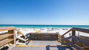A wooden boardwalk leading to a beach with white sand and clear blue water.