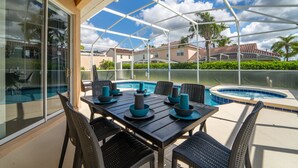 Um pátio externo com mesa e cadeiras, piscina e vista para casas vizinhas.