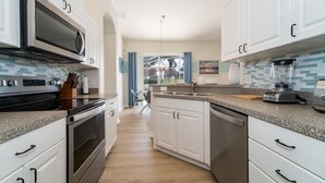 Uma cozinha moderna com armários brancos, eletrodomésticos de aço inoxidável e painel de azulejos.