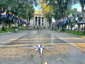 A courtyard with a central star-shaped sculpture, surrounded by rows of flags and a building with columns in the background.