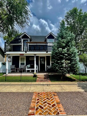 A two-story house with a balcony, a front porch with chairs, and a fenced yard.
