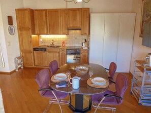 A dining area with a round table, six chairs, and a kitchen in the background.