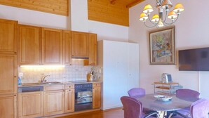 Eine moderne Küche mit Holzschränken, einem eingebauten Backofen und einem Essbereich mit violetten Stühlen und einem Glastisch.