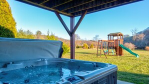 Un bain à remous sous une pergola en bois, avec un terrain de jeux en arrière-plan.