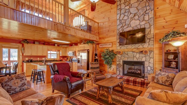 Un intérieur de chalet spacieux, doté d’une cheminée en pierre, d’un coin repas en bois et d’un espace salon confortable avec des fauteuils en cuir.