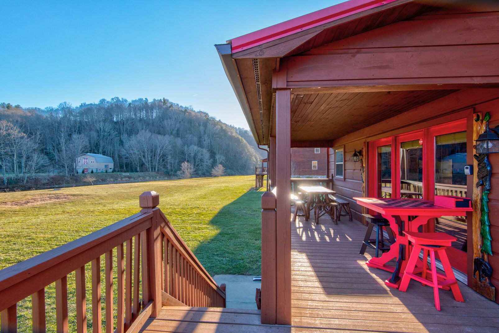 Une terrasse en bois avec une table et des chaises, d’où l’on peut admirer un champ verdoyant et une montagne au loin.