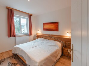 Et soveværelse med en seng, et vindue med gardiner, en radiator, et sengetæppe med en lampe og et billede på væggen.