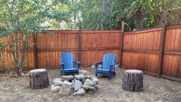 Ein Garten mit zwei blauen Adirondack-Stühlen, einer Feuerstelle und einem Holzzaun.